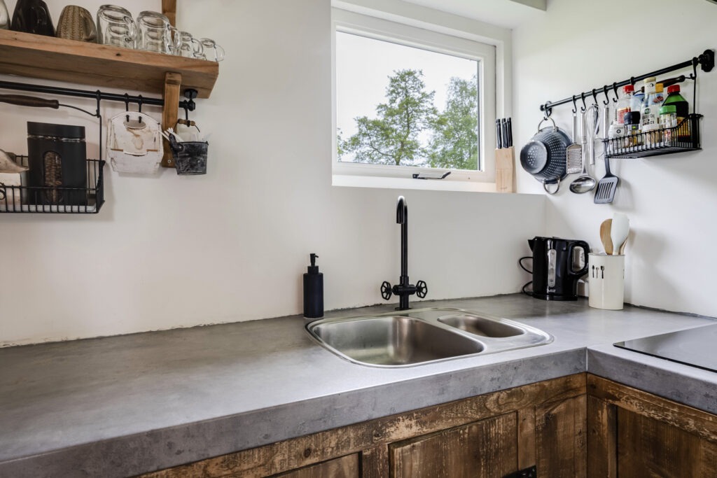 Op deze foto zie je de keuken van de Boerenlodge. De kastjes zijn van hout. Het aanrecht heeft een grijze natuurstenen look.